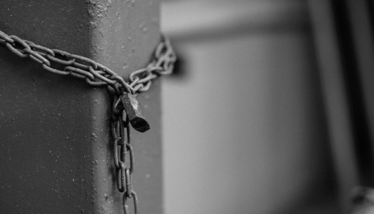 Close-up of a rusty chain with a padlock securing a steel post in monochrome tones.