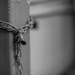 Close-up of a rusty chain with a padlock securing a steel post in monochrome tones.
