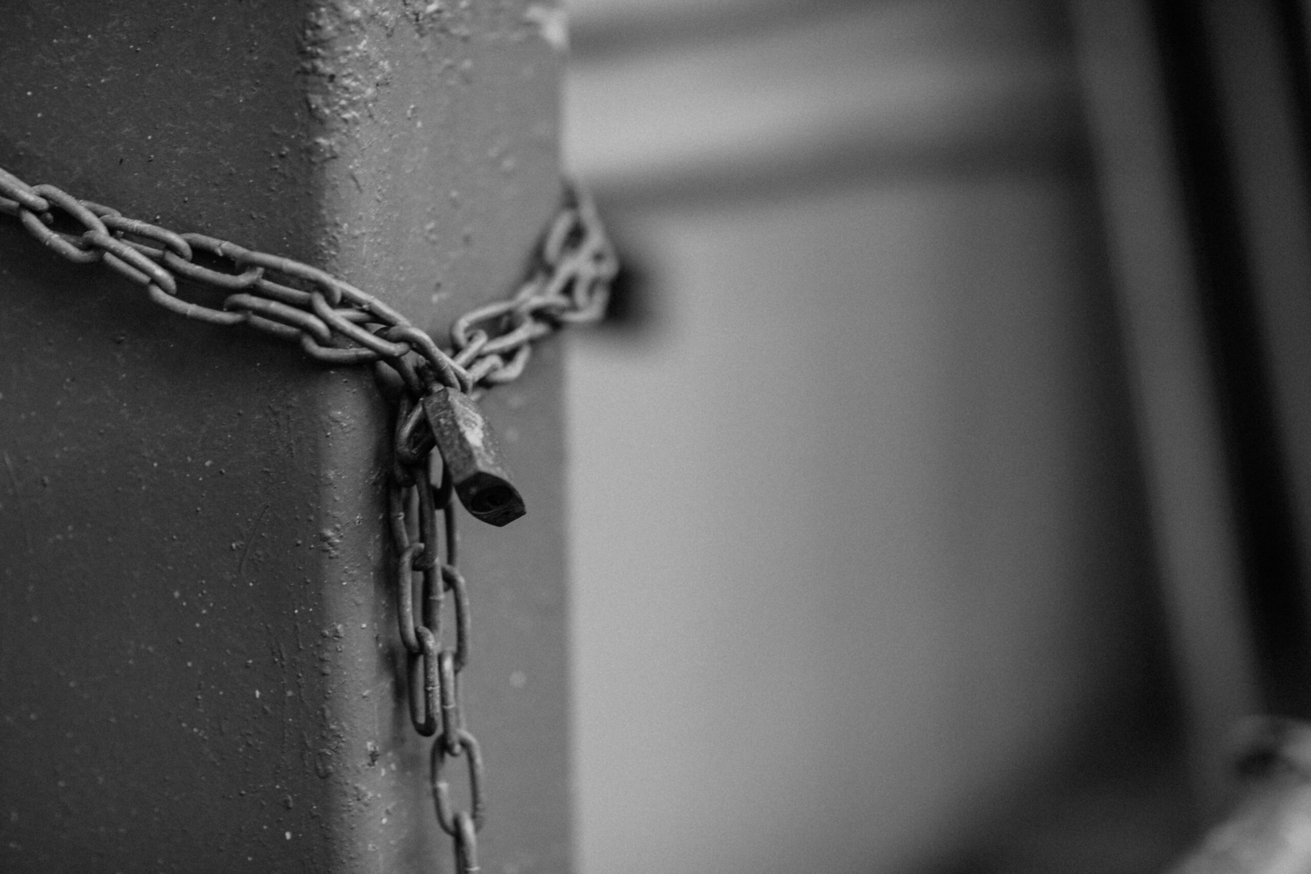 Close-up of a rusty chain with a padlock securing a steel post in monochrome tones.