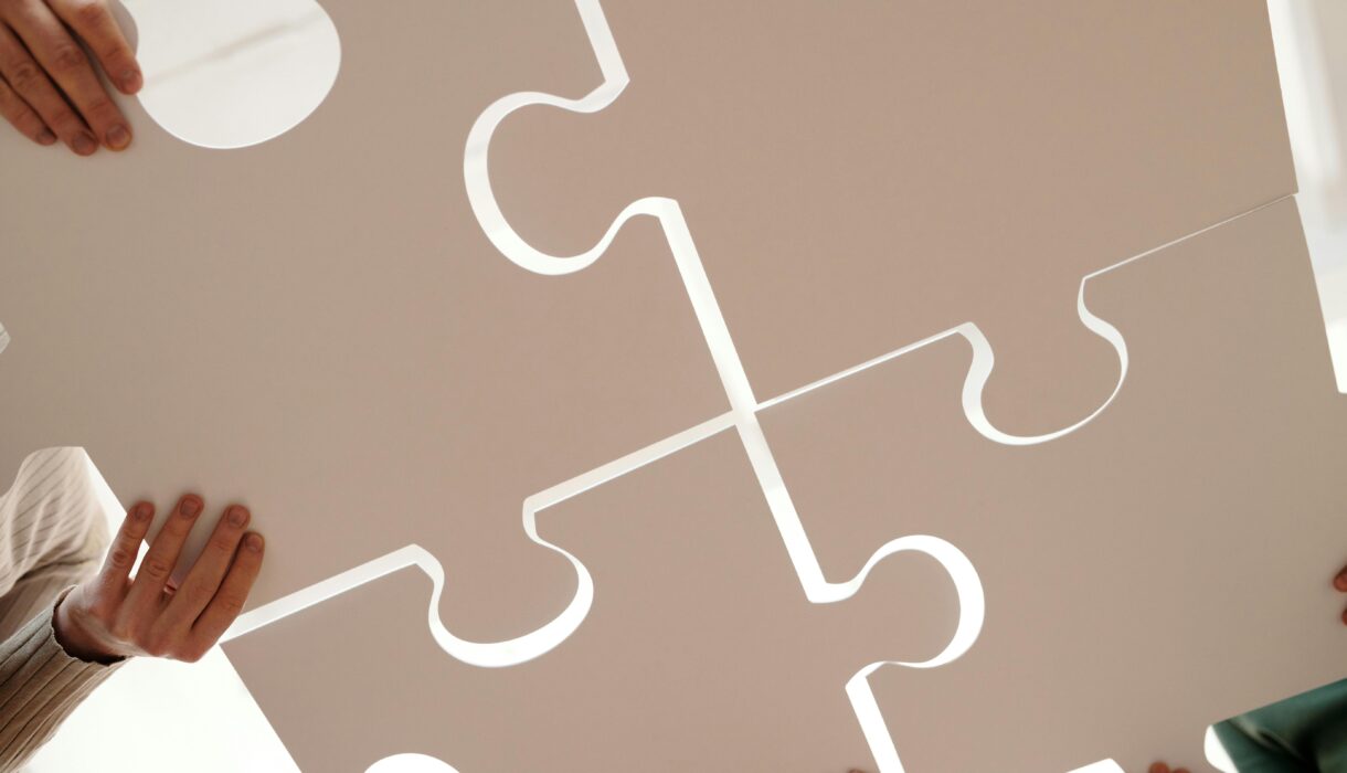 Hands of diverse individuals holding large puzzle pieces, symbolizing teamwork and unity.